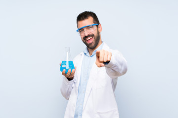 Young scientific holding laboratory flask over isolated background points finger at you with a confident expression