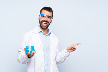 Young scientific holding laboratory flask over isolated background pointing to the side to present a product