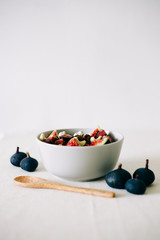 a plate of healthy Breakfast with oatmeal, figs and cashew nuts on a white table with a bamboo spoon. vegan food