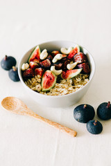 a bowl of healthy Breakfast with oatmeal, figs and cashew nuts on a white table with a bamboo spoon. vegan food