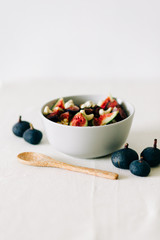 a bowl of healthy Breakfast with oatmeal, figs and cashew nuts on a white table with a bamboo spoon. vegan food