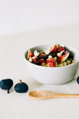a bowl of healthy Breakfast with oatmeal, figs and cashew nuts on a white table with a bamboo spoon. vegan food