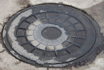 one old and wet iron sewer manhole lies on gray asphalt on the street