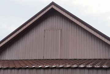 part of a rural house with a brown wooden attic with a closed door against a gray sky