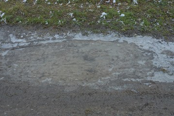 gray puddle with frozen ice on the ground near the green grass on the street
