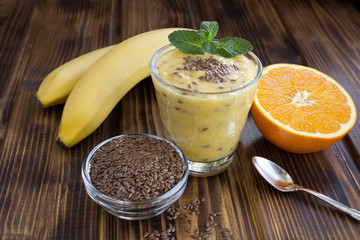 Smoothies with flax seeds, orange and banana  in the glass on the brown wooden  background. Closeup.