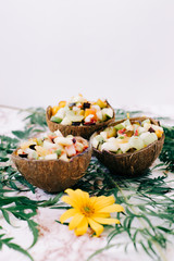 healthy fruit salad in a bowl of coconut shells on the table with tropical leaves. vegetarian food