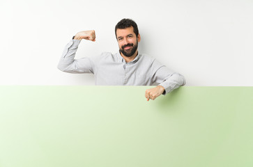 Young handsome man with beard holding a big green empty placard doing strong gesture