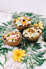 healthy fruit salad in a bowl of coconut shells on the table with tropical leaves. vegetarian food