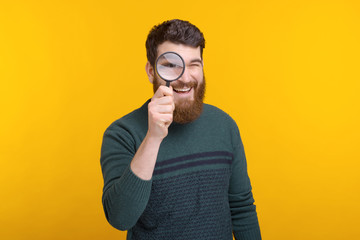 man looking through magnifying glass while standing over yellow background