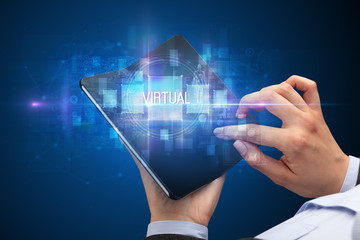 Businessman holding a foldable smartphone with VIRTUAL inscription, new technology concept