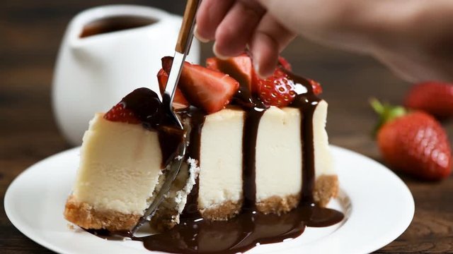 Taking bite of cheesecake with fork. Eating New York Cheesecake with strawberries and chocolate sauce