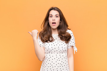 young pretty woman looking astonished in disbelief, pointing at object on the side and saying wow,...