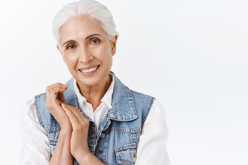 Close-up portrait pleasant, charming old modern lady, senior woman with grey hair in stylish denim vest, touching hands, apply daily anti-aging creme, taking care skin cosmetology products, smiling