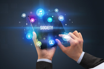 Businessman holding a foldable smartphone with SOCIETY inscription, social media concept