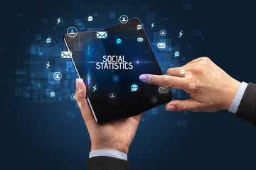 Businessman holding a foldable smartphone with SOCIAL STATISTICS inscription, social networking concept