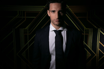 Handsome man in suit and tie in front of art deco backdrop smiling at camera