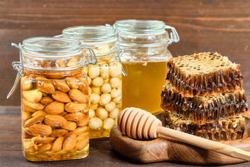 honey in honeycombs on a wooden plate and golden honey in jars with nuts