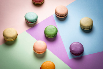 Fototapeta na wymiar Colorful macaroons on creative geometric pastel background. Variety of french almond macaron cookies on multicolor backdrop. Dessert, sugar, bakery concept. Macro shot, overhead view, close up