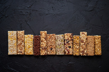 Various healthy granola bars placed in a row on black stone table