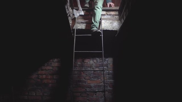 a man with an ax and rubber boots, descends the iron stairs to the basement of red brick in stamp.