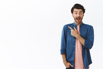 Surprised, astonished handsome bearded man in pink t-shirt, shirt, pointing upper left corner,...