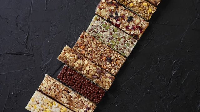 Various healthy granola bars placed in a row on black stone table