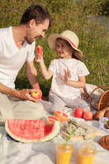 Dad and daughter eat watermelon sitting on the grass during a picnic in the park