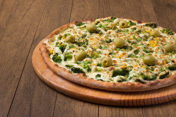 Delicious Broccoli Pizza served on wooden board. Baked with mozzarella, broccoli, corn, peas, olives and sauce. Olive oil, basil, Pizza on the right.