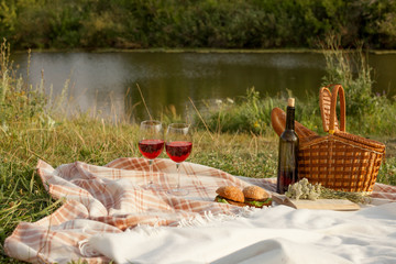 Romantic picnic at sunset. Picnic basket with red wine, bread
