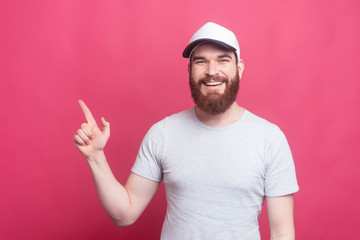 Joyful handsome man pointing at copyspace over pink background