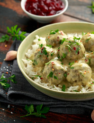 Hot Swedish meatballs with white rice and cranberry sauce on wooden table
