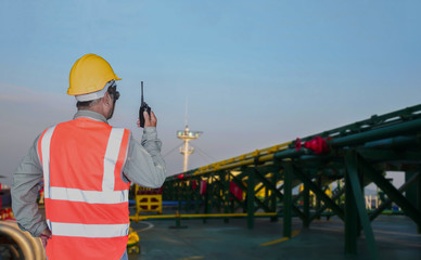 worker with walkie talkie in hand On deck of oil tanker ship with pipe line connect while the ship is at sea on green pipe line background.