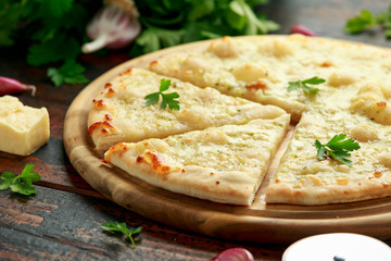 Garlic cheese pizza on wooden board with herbs.