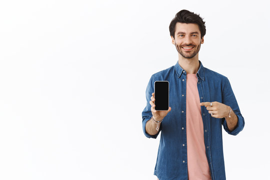 Pleased, confident cheeky bearded man bragging, showing photos on smartphone, holding phone, pointing mobile display and grin satisfied, recommend good online store, white background