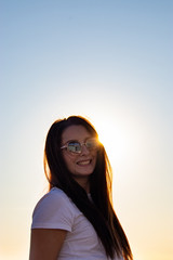 Fototapeta premium Attractive brunette with sunglasses laughing , sun directly behind her head peeking, golden sunset hour.