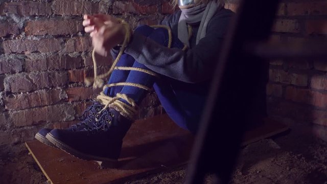 woman trying to free her hands from the rope. Sits in the basement, Close-up.