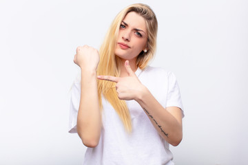 young pretty blonde woman looking impatient and angry, pointing at watch, asking for punctuality,...