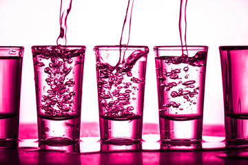 Vodka shots in a row. Neon pink bar encounter. Illuminated transparent glass. Pouring liquor....