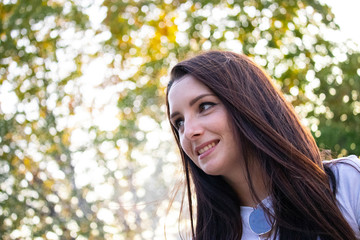Young brunette smiling looking into the distance , green white background bokeh on a warm summer day.