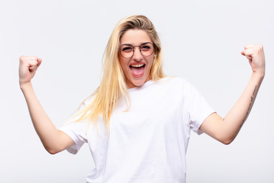 young pretty blonde woman feeling happy, surprised and proud, shouting and celebrating success with a big smile against white wall