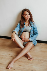 Luxurious young mother posing sitting on the floor. Girl expecting a baby. Hold belly with hand.