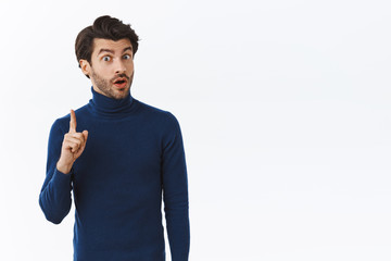 Handsome bearded man in blue high neck sweater raise one finger and sharing his thought, suggest something during office meeting, give advice or recommend product, standing white background