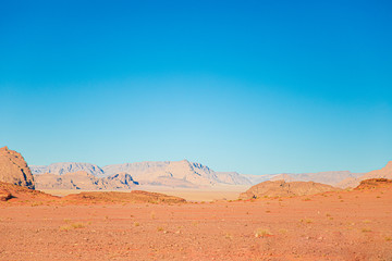 Sandy landscape with red and orange Sandstone mountains against a blue sky, Jordan, Wadi Rum desert.