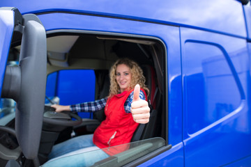 Portrait of professional truck driver showing thumbs up and smiling. Truck vehicle in background....
