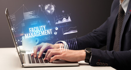 Businessman working on laptop with FACILITY MANAGEMENT inscription, new business concept