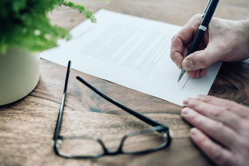 close-up of businessman signing contract or document at rustic wooden table.