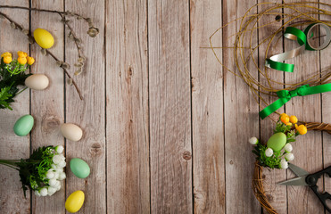 Easter composition. Making an Easter wreath. Willow branches, eggs, scissors, flowers, ribbons, bow and thread on a wooden background. Free space.