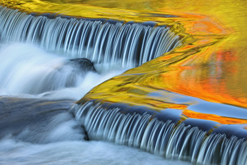 Panele Szklane  Kaskada Bond Falls uchwycona z rozmyciem ruchu i oświetlona odbitymi kolorami od oświetlonych słońcem jesiennych klonów i błękitnego nieba nad głową, górny półwysep Michigan, USA