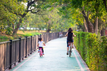 Back view of happy asian mother and daughter riding on bicycle in the city park , resting on holiday , health lifestyle concept.